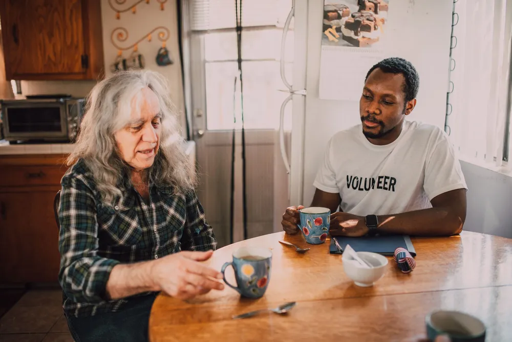 A caregiver shares tea and conversation with a senior woman at her kitchen table